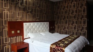 A hotel room with a large bed, a wooden nightstand, and a patterned wall. - Yabuli Skier Hotel (Harbin)