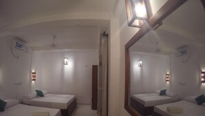 Une chambre d’hôtel avec deux lits simples, un banc en bois, un grand miroir et des lampes fixées au mur.
