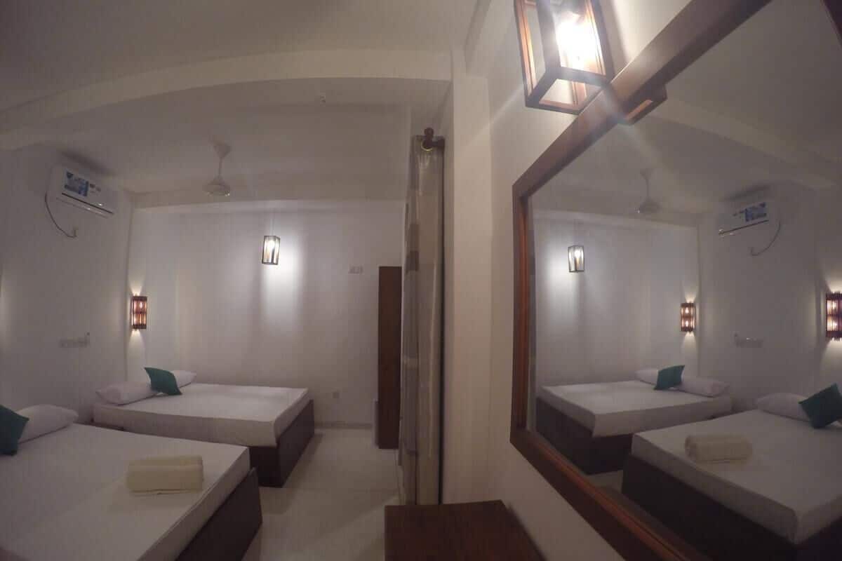 A hotel room with two single beds, a wooden bench, a large mirror, and wall-mounted lights.