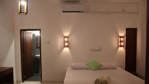 Une chambre d’hôtel comprenant un lit, deux lampes fixées au mur, un appareil de climatisation et une porte donnant accès à une salle de bain.