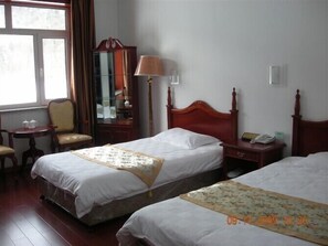 A hotel room with two beds, a bedside table with a lamp, a chair, a small table with cups, and a mirror. - Yabuli Olympic Club Hotel (Harbin)