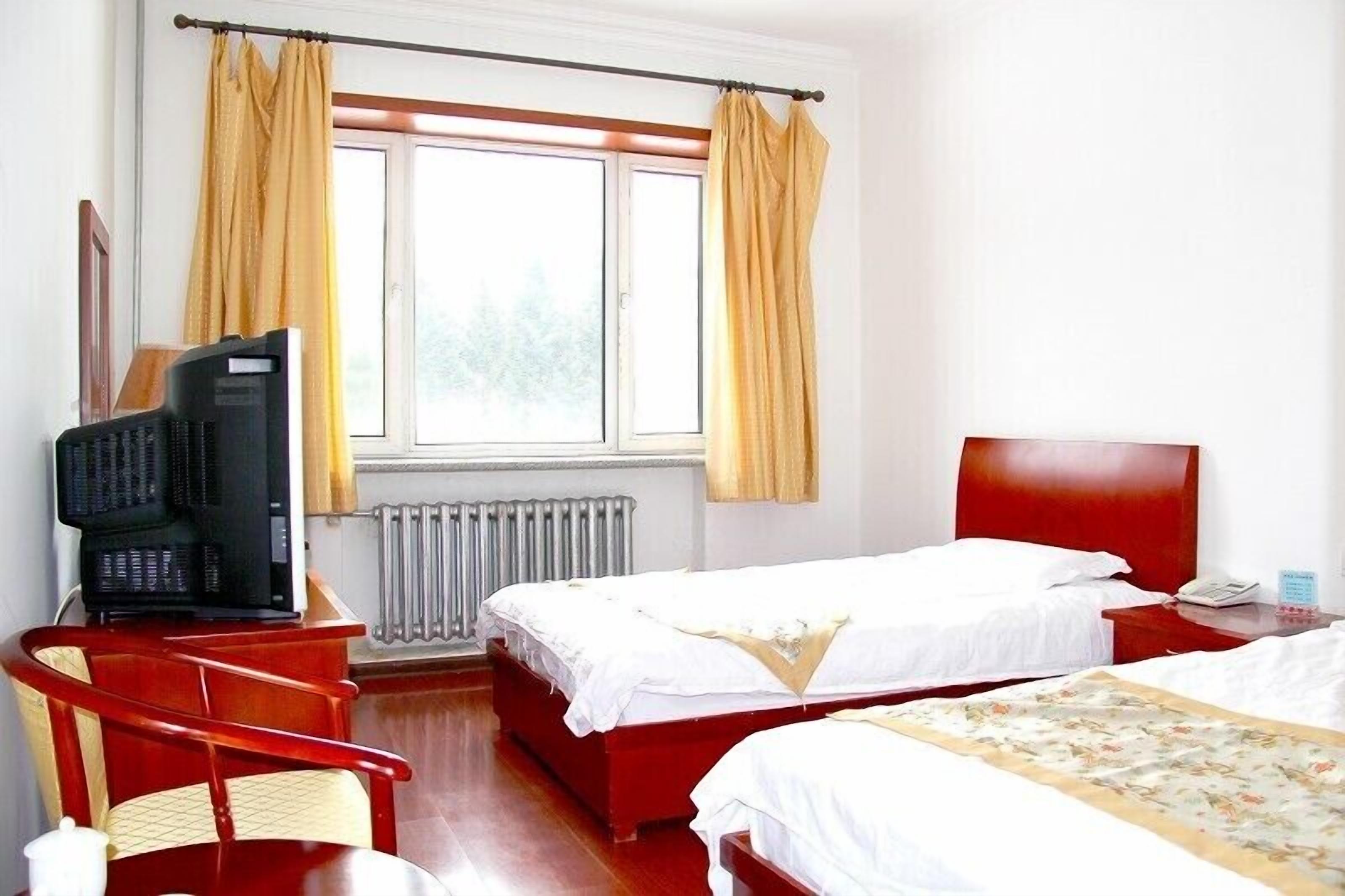 A hotel room with two beds, a television, a radiator, and a window with curtains.