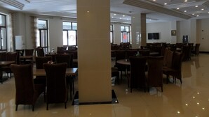 Un comedor amplio con varias mesas y sillas, ventanas grandes y un piso pulido.