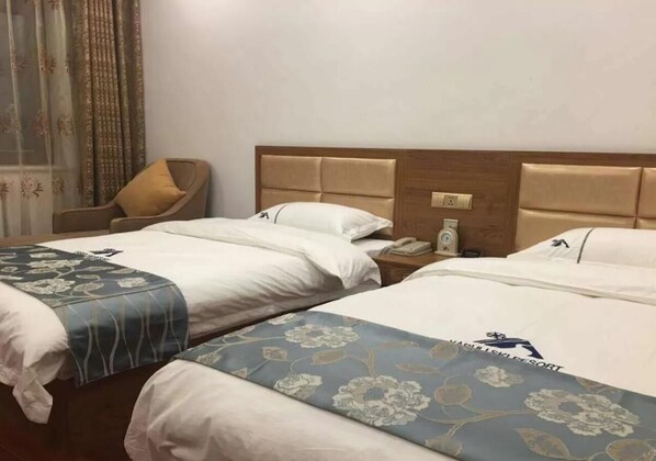 A hotel room with two beds, a wooden headboard, a bedside table with a phone, and a chair.