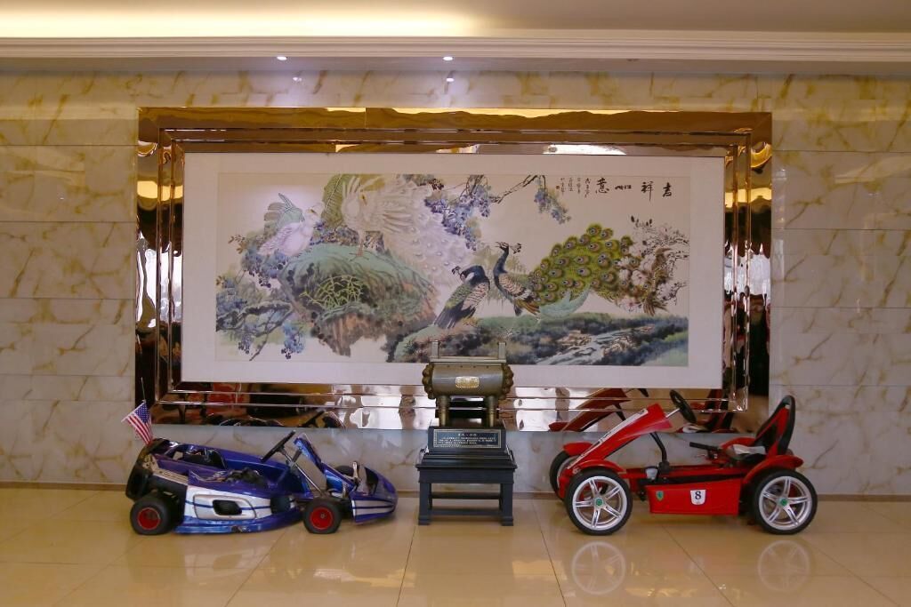 A room with a large painting on the wall, a small table with a plaque, and three toy cars in front.
