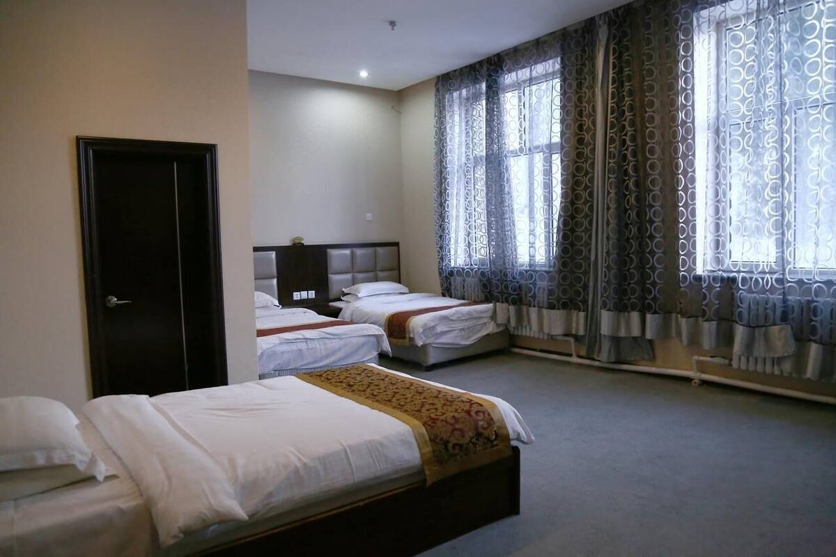 A hotel room with two single beds, a dark-colored wardrobe, and a large window with patterned curtains.
