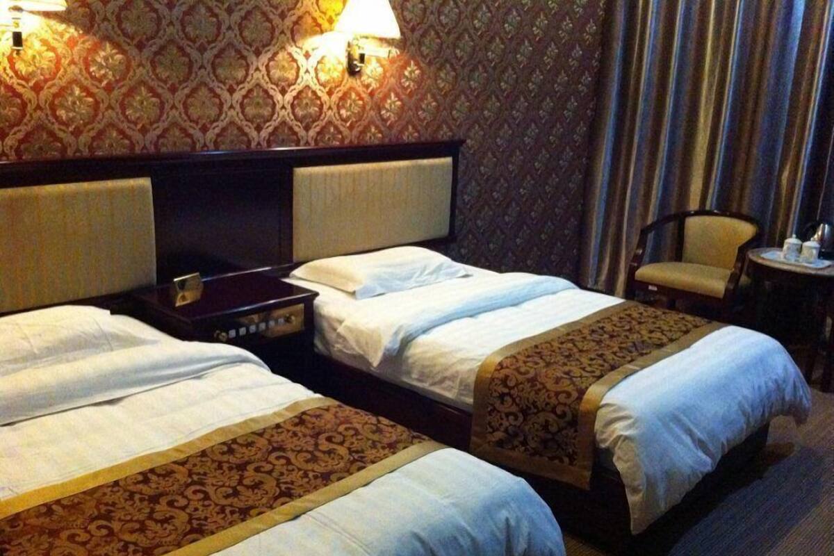 A hotel room with two beds, a wooden headboard, a small table with a lamp, and a chair.