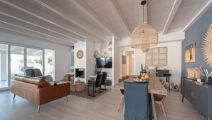A modern living room with a sofa, dining table, and chairs. There is a television and a decorative wall piece.