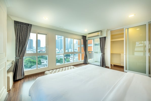 Habitación de hotel con una cama grande, un vestidor amplio y vistas de la ciudad a través de ventanales.