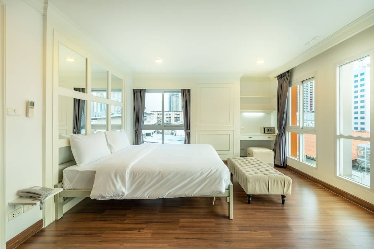 A modern hotel room with a large bed, a bedside table, a desk, and a view of the city through large windows.