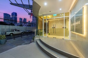 A modern hotel entrance with a glass facade, a staircase leading to the entrance, and a cityscape view in the background. - Le Grande City Pratunam (Bangkok)