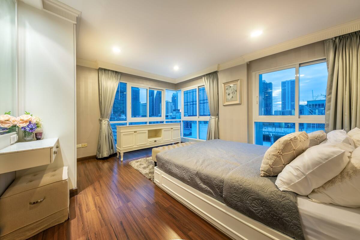 A modern bedroom with a large bed, a vanity, and a view of the cityscape through large windows.