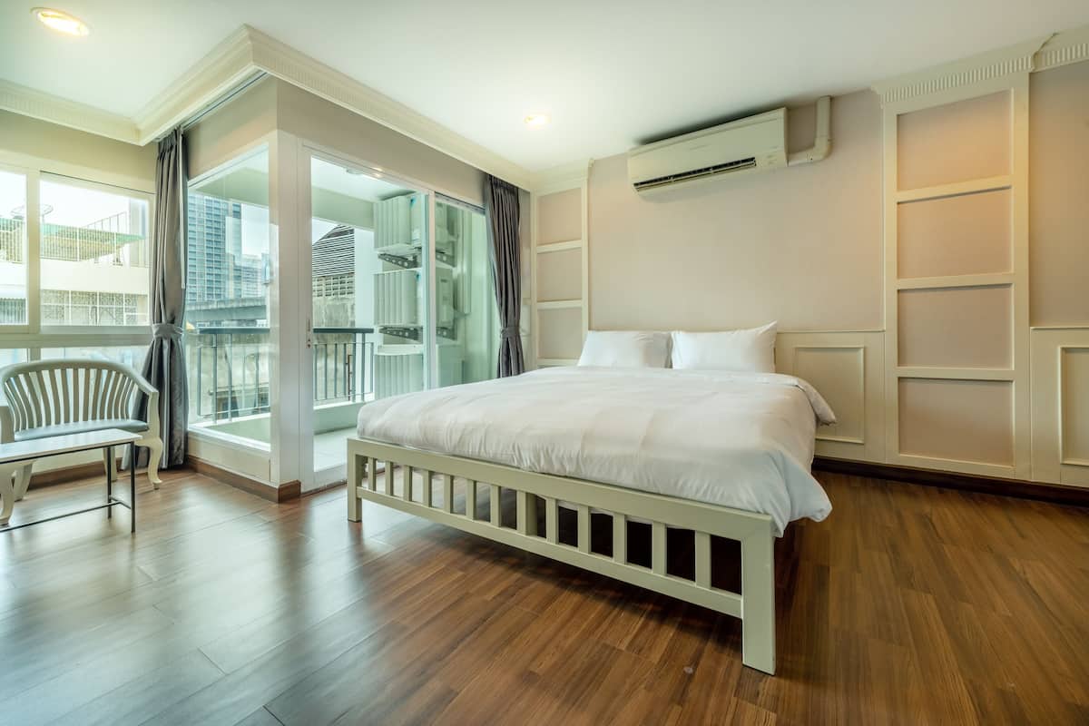 A bedroom with a bed, a chair, a balcony, and a view of buildings.