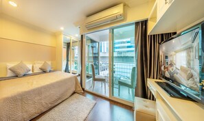 A hotel room with a bed, a TV, a balcony with a view of buildings, and an air conditioning unit. - Le Grande City Pratunam (Bangkok)