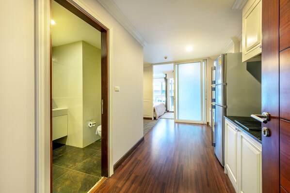 A hallway with wooden flooring, a kitchen area with a refrigerator, and a bathroom with a toilet and sink.