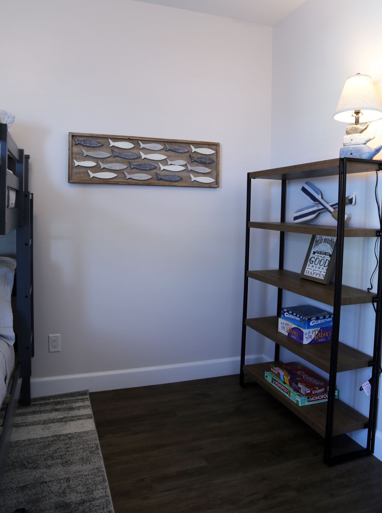 A room with a wooden fish wall art, a metal shelf with board games, and a lamp on the right.