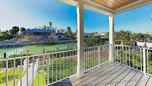 Ein überdachter Außenbereich mit Holzterrasse, weißen Geländern und Blick auf ein Gewässer sowie Gebäude im Hintergrund.