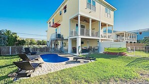 Ein zweistöckiges Haus mit überdachter Terrasse, Schwimmbad und Gartenmöbeln.