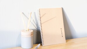 A notebook, a pen, and a container with wooden sticks on a wooden surface. - Seven77 (Tainan)
