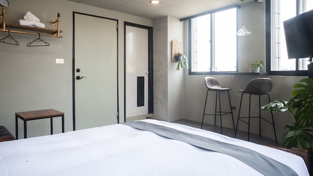 A hotel room with a bed, a small table, two bar stools, a TV, and a window with natural light. - Seven77 (Tainan)