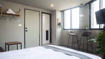 Habitación de hotel con cama, una mesita, dos taburetes, televisión y ventana con luz natural.