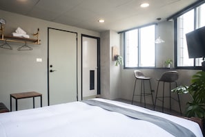 Habitación de hotel con cama, una mesita, dos taburetes, televisión y ventana con luz natural.