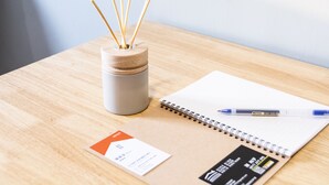 A wooden table with a notebook, a pen, a small container with reed sticks, and a business card. - Seven77 (Tainan)
