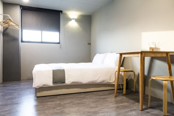 Un dormitorio minimalista con una cama, una mesita de madera y una percha para ropa.