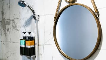 Un baño con ducha, un espejo redondo con asa de cuerda y dos vasos de vidrio en una estantería.