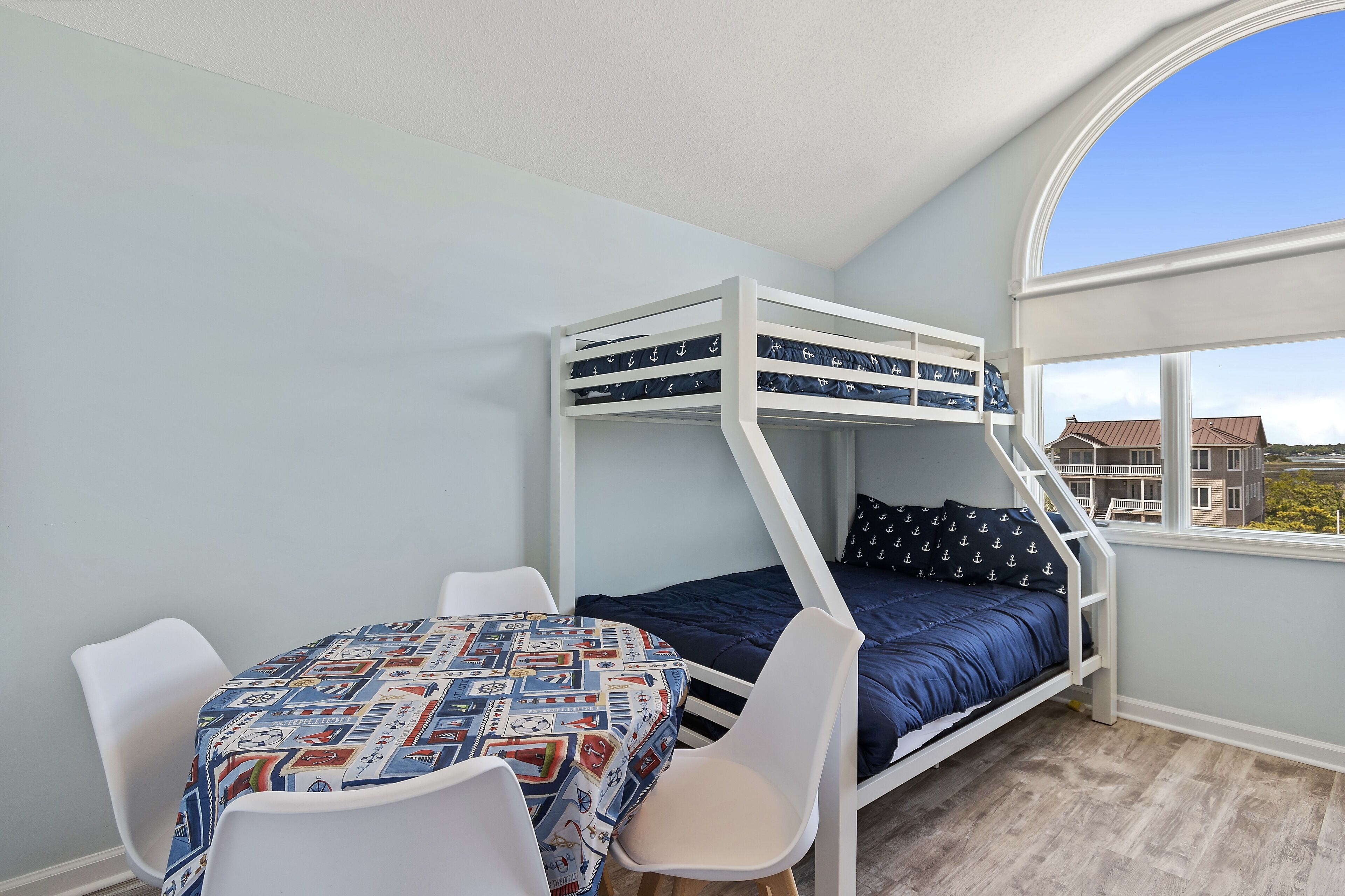 Un letto a castello con tavolo e sedie decorate, una finestra che mostra edifici e una parete azzurra.