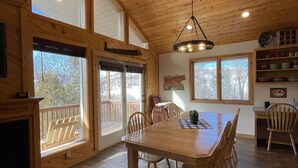 Un comedor amplio con una gran mesa de madera y sillas, una chimenea y ventanas grandes que ofrecen vistas al exterior.