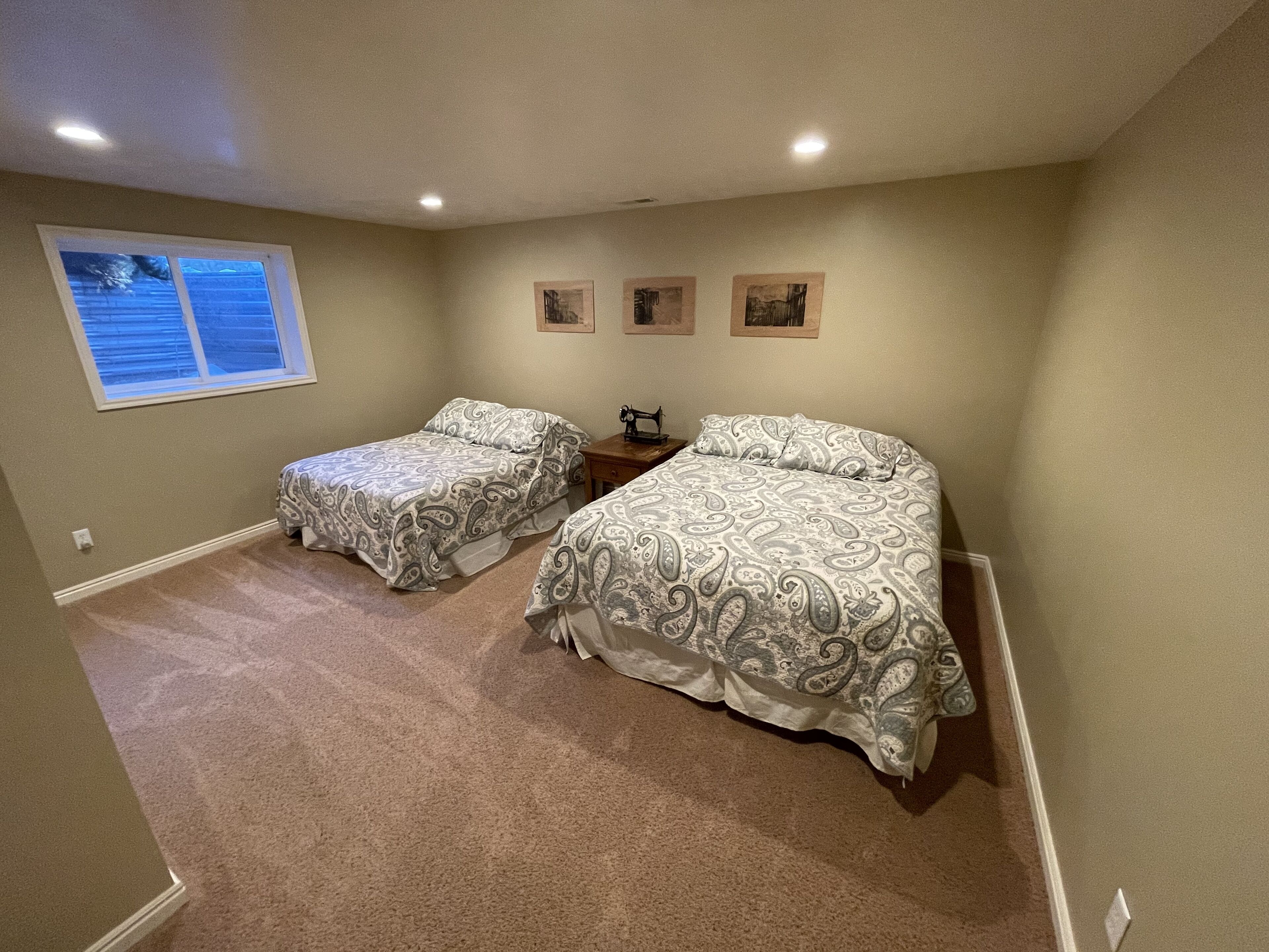 A bedroom with two beds, a window, and a small table with a sewing machine.