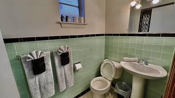 Un baño con azulejos verdes, un inodoro, un lavabo y toallas colgadas en la pared.