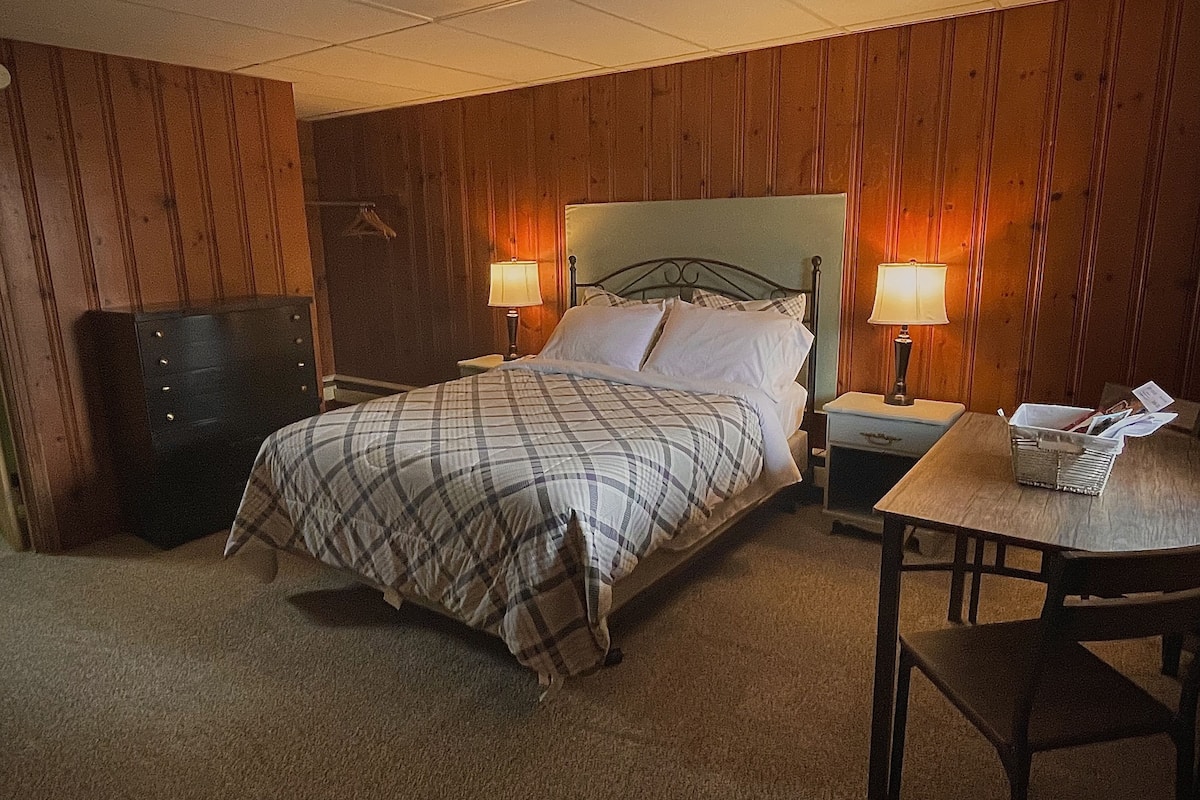 A bedroom with a bed, two bedside tables with lamps, a dresser, and a small table with papers.