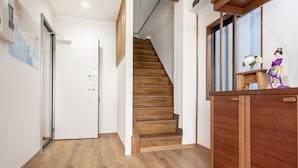 Een houten trap die naar een verdieping leidt, een houten bureau met een decoratief object, en een witte deur met een kaart op de muur.