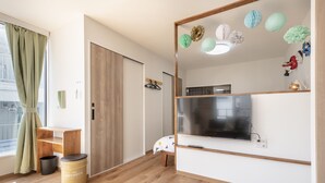 Een moderne kamer met een houten vloer, een aan de muur bevestigde televisie, een klein houten bureau en een groen gordijn.