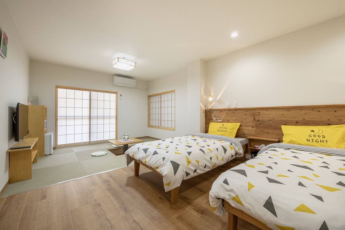 Une chambre d’hôtel avec deux lits, une tête de lit en bois, un bureau avec une chaise, une télévision et une fenêtre donnant sur un paysage agréable.