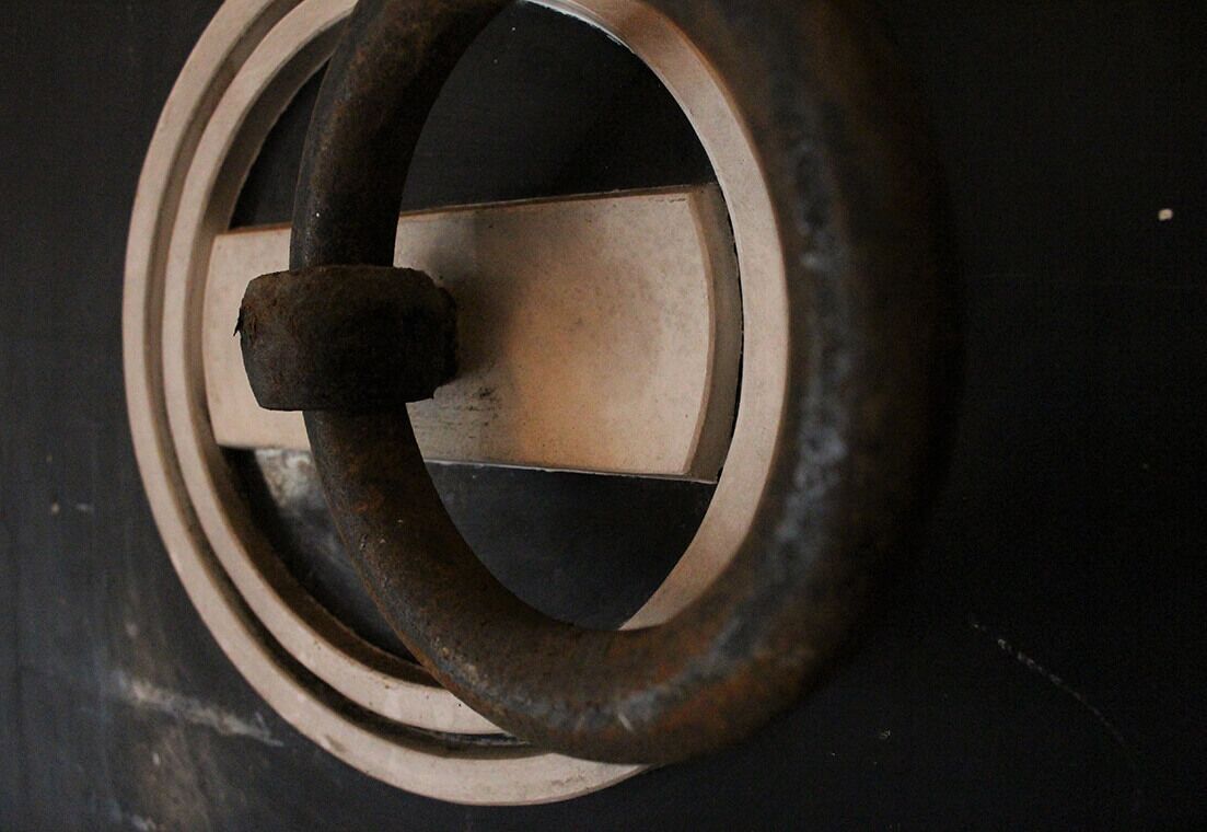 Gros plan d’un objet métallique circulaire doté d’une section rectangulaire centrale, qui pourrait être une pièce d’un mécanisme de porte ou de fenêtre.