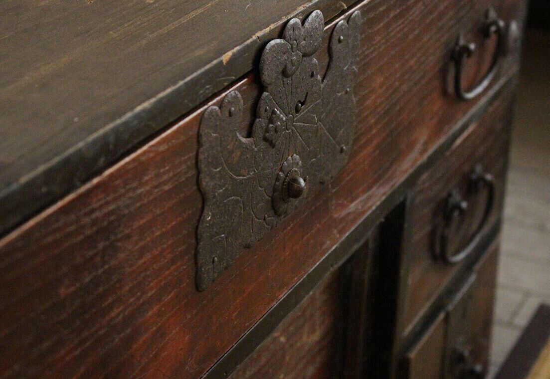 A close-up of a wooden dresser with ornate metal handles and a decorative metal plate.