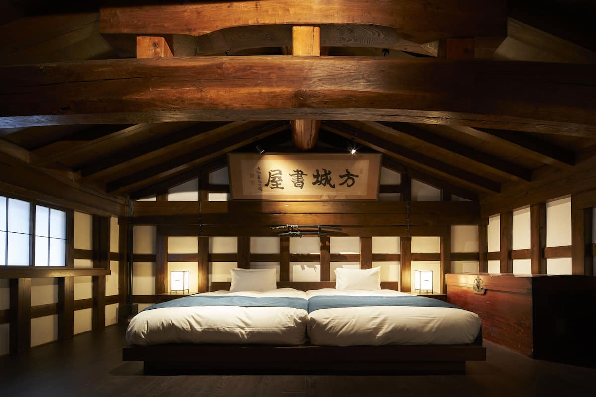 Ett traditionellt japanskt sovrum med ett träpanelat tak, golvbeläggning av tatamimattor och en säng med vita sängkläder.