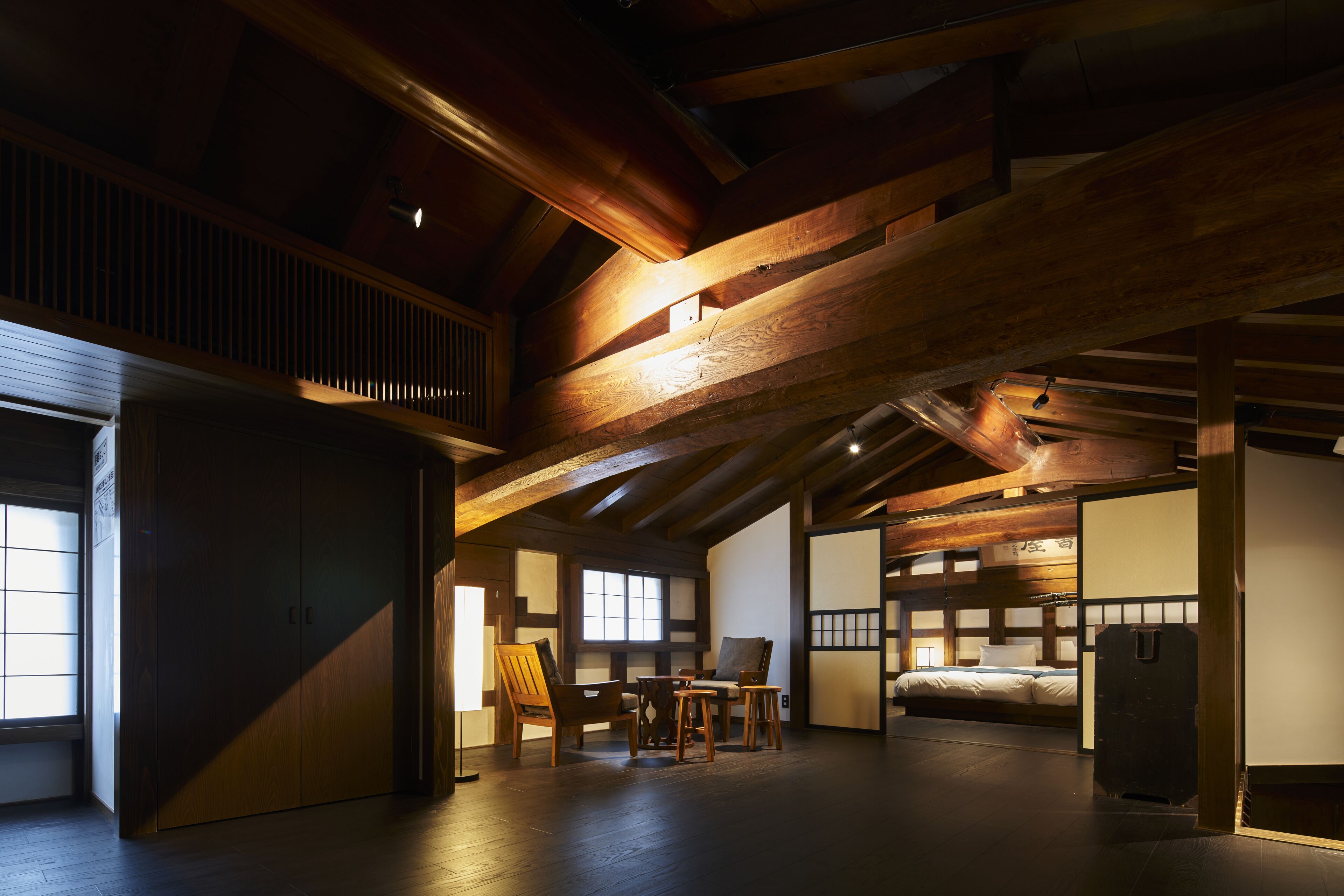 Una habitación tradicional japonesa con suelo de tatami, techo bajo con vigas a la vista, una puerta corredera y una cama con futón.