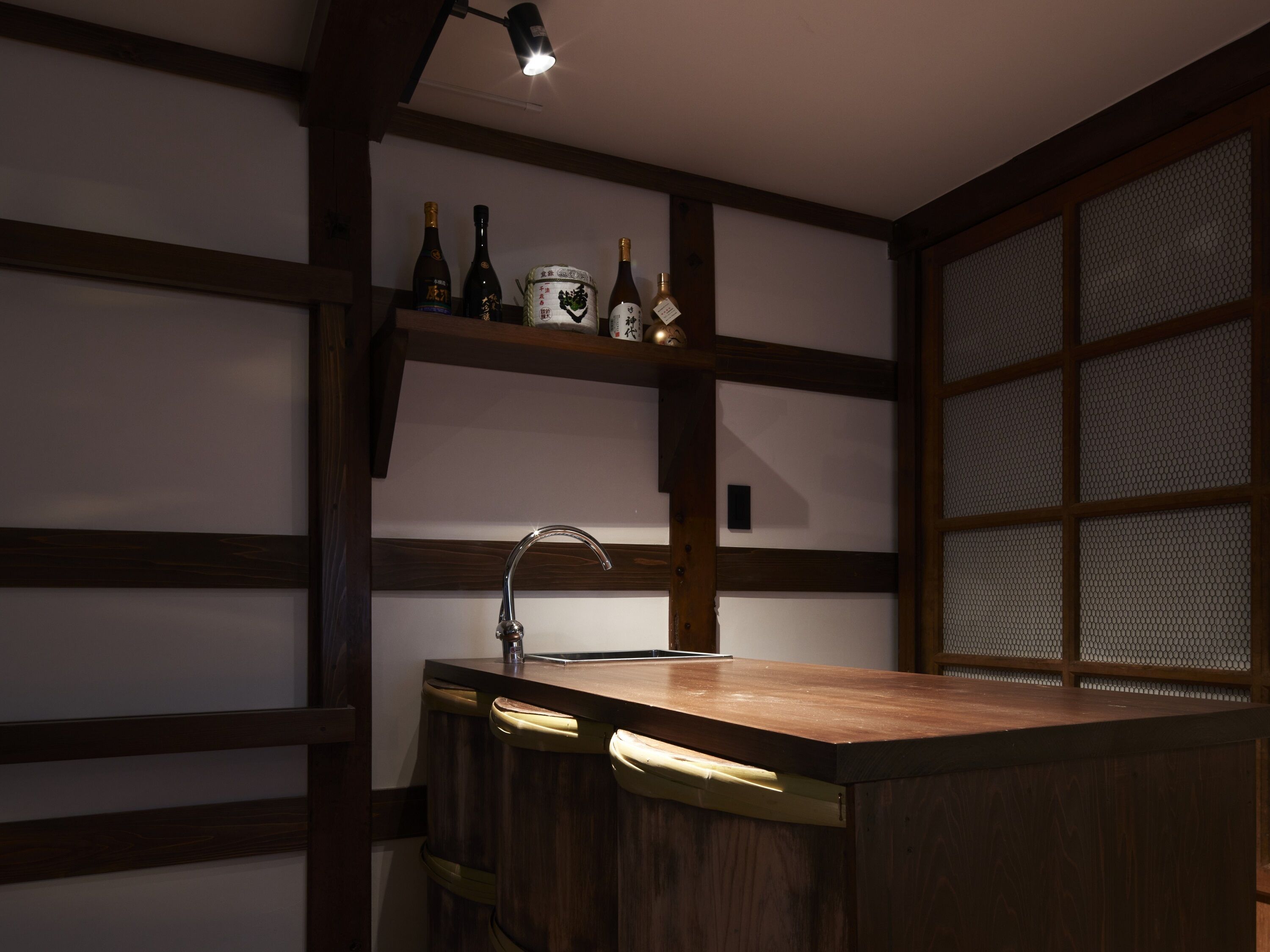 A kitchen with a wooden counter, a sink, and a shelf with bottles.