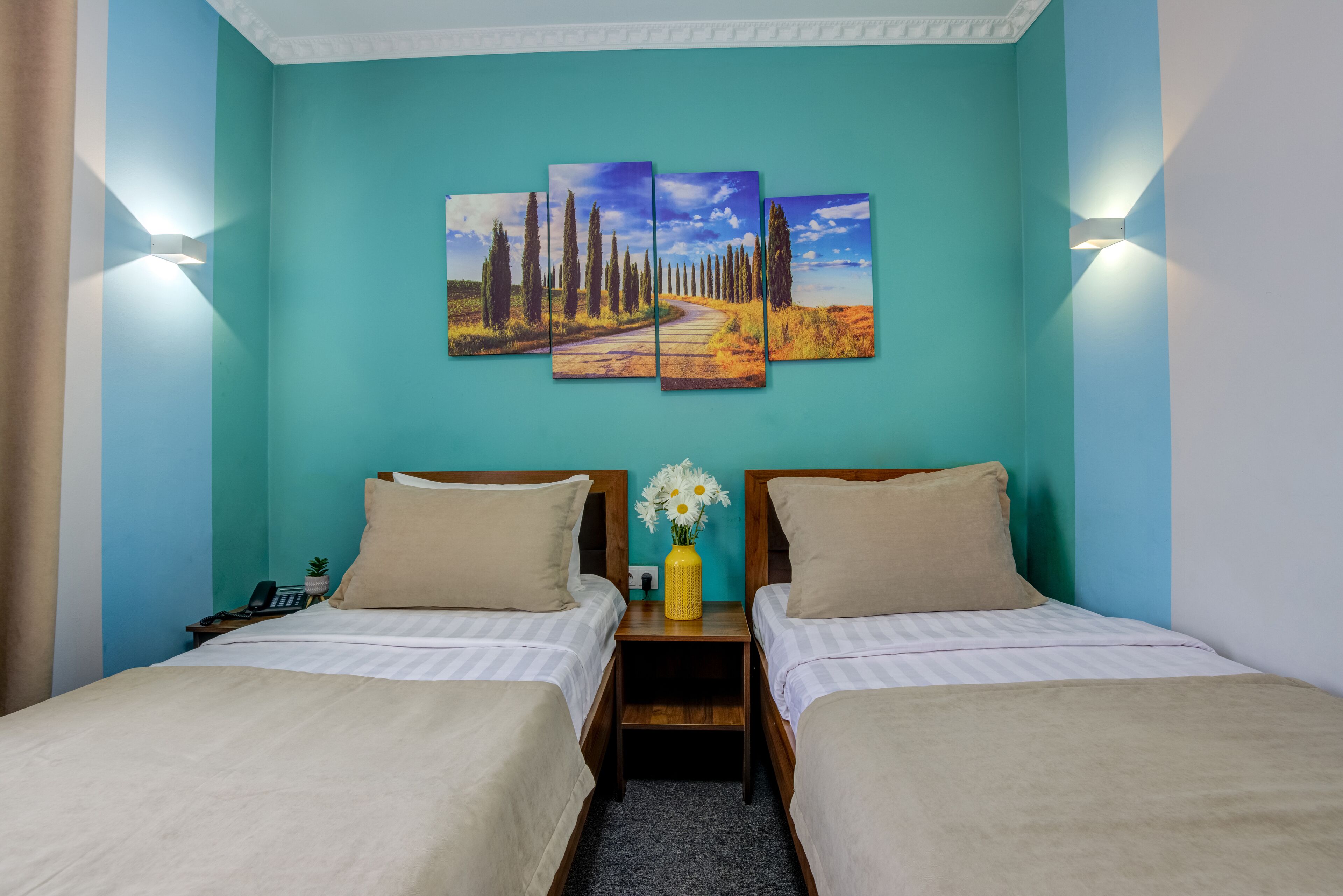 A hotel room with two beds, a nightstand, a vase with flowers, and a wall-mounted painting.