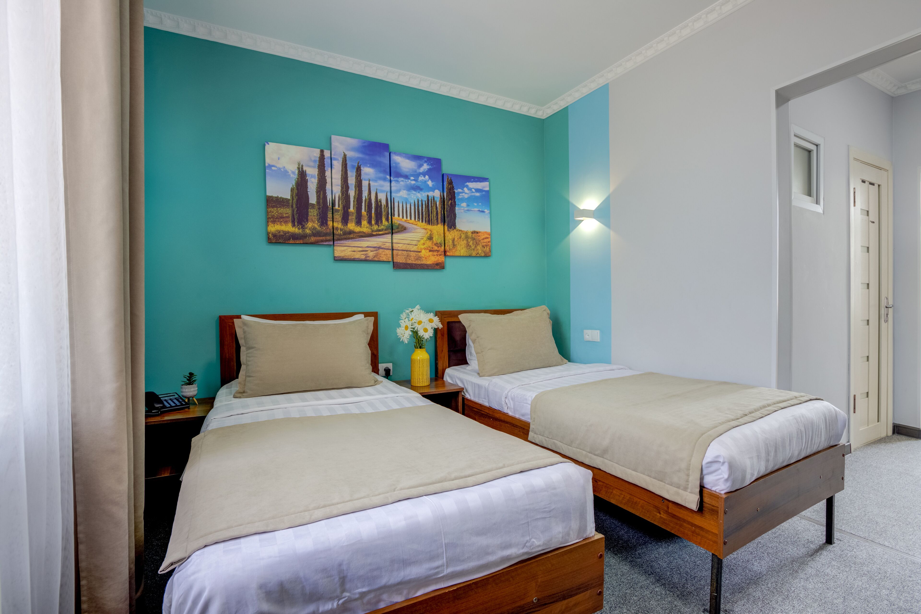 Een kamer met twee eenpersoonsbedden, een wand in een blauwgroene kleur en een landschapsschilderij boven de bedden.
