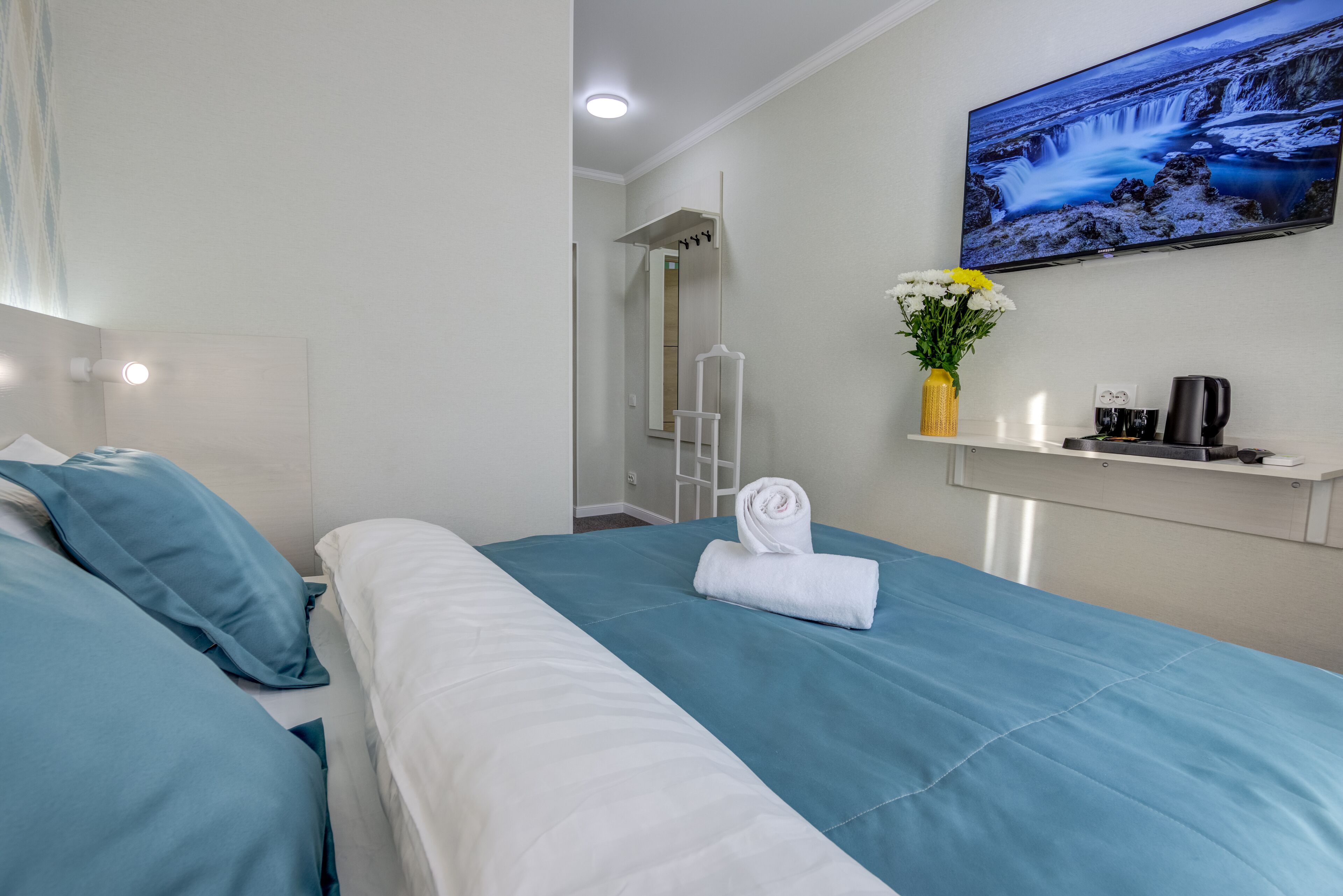 A hotel room with two beds, a TV mounted on the wall, a small table with a vase of flowers, and a coffee machine.