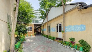 Un étroit sentier bordé de plantes en pot et un bâtiment sur lequel on peut lire l’inscription « Cuisine ».