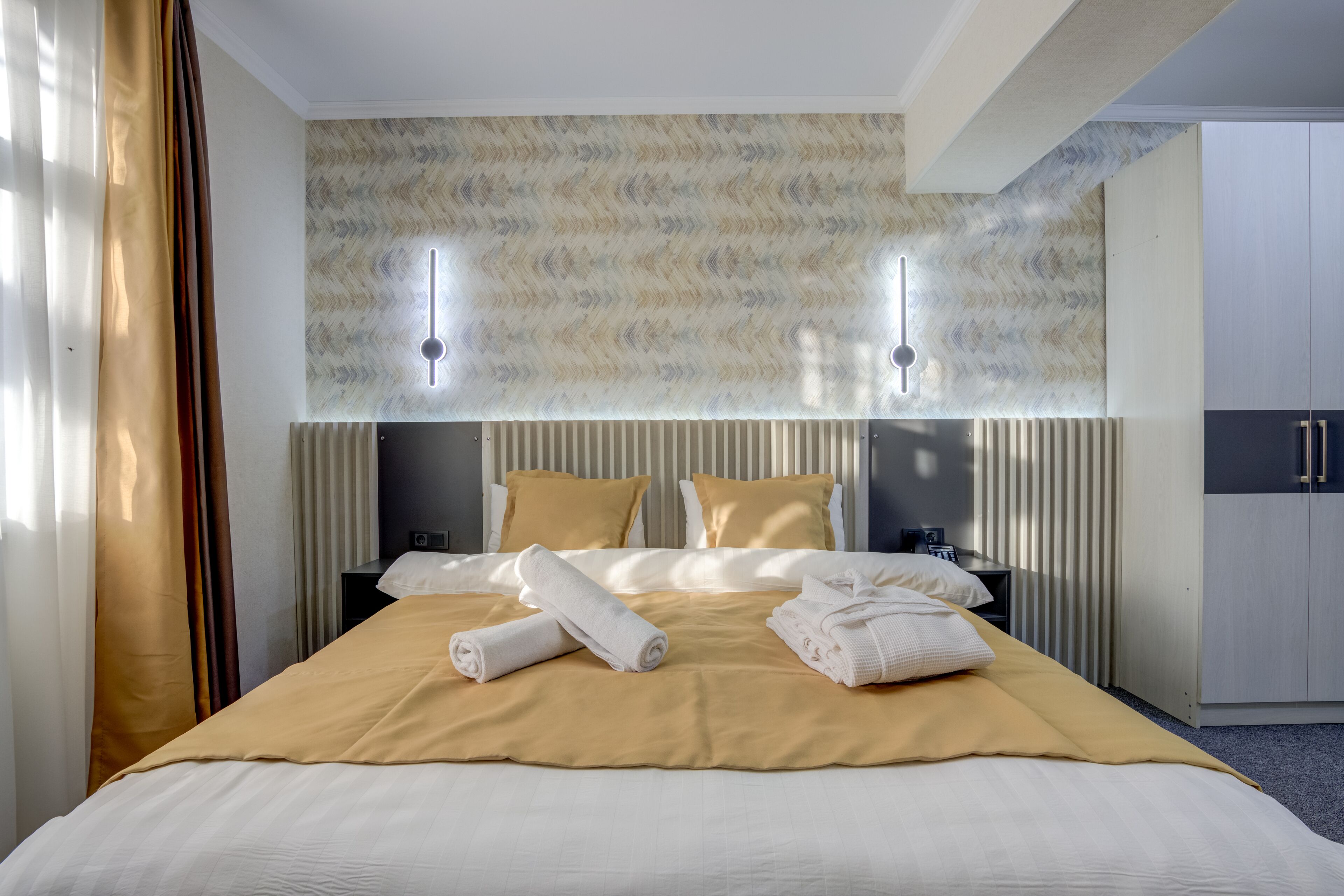 A hotel room with a large bed, two bedside tables, a wardrobe, and a wall-mounted light fixture.