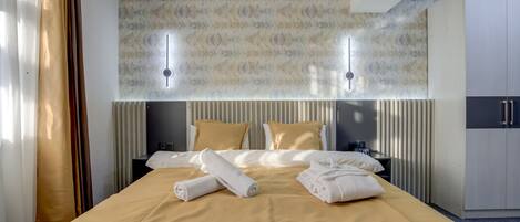 A hotel room with a large bed, two bedside tables, a wardrobe, and a wall-mounted light fixture.