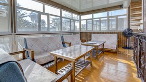 Une véranda avec un plancher en bois, de grandes fenêtres et un ventilateur.