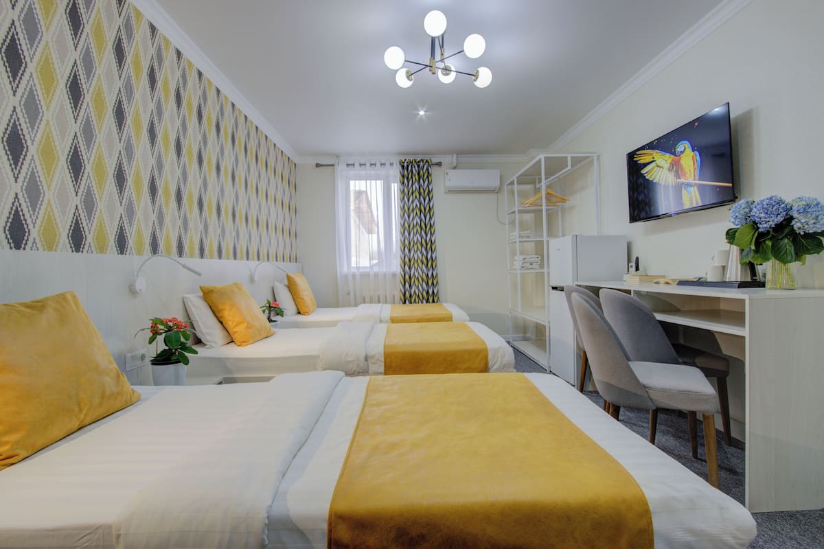 Habitación de hotel con dos camas, un escritorio, una silla, un televisor y un ventanal con cortinas.